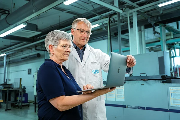 Zwei Mitarbeitende prüfen Fertigungsdaten auf einem Laptop in der Produktionshalle