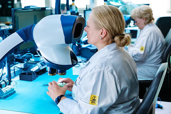 Mitarbeiterin kontrolliert eine Leiterplatte an einem optischen Prüfgerät